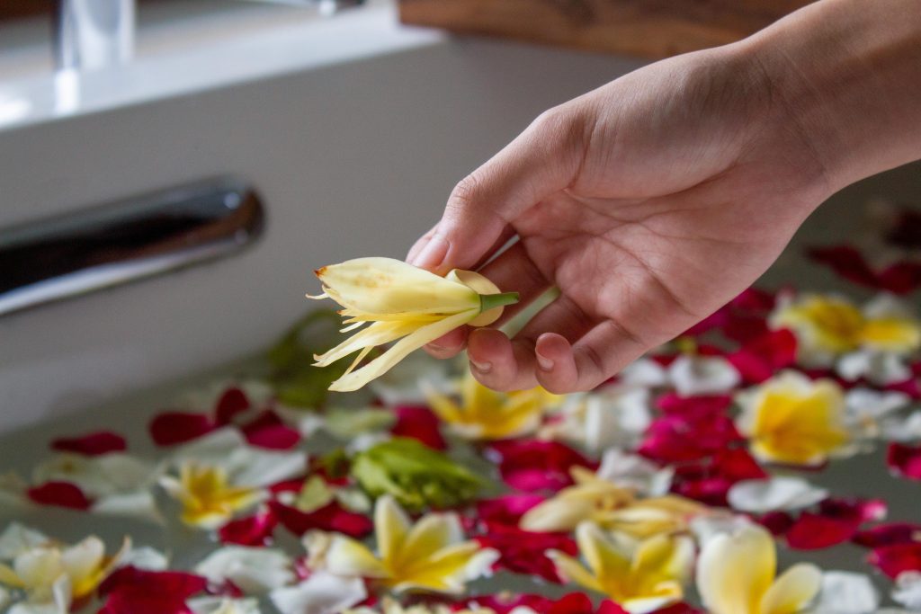 Hand placing fresh flowers into a bathtub filled with water and petals, creating a romantic hot tub atmosphere